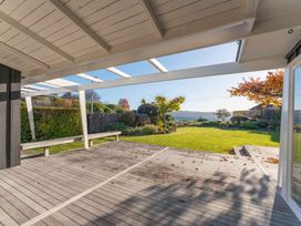 Covered outdoor wooden deck leading to a lawn with trees and shrubs at Waterside Bliss - Taupo Holiday Home Taupo Central