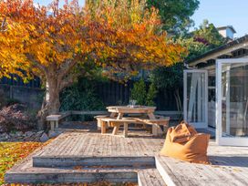 An outdoor wooden deck with a table and benches under a tree with orange leaves at Waterside Bliss - Taupo Holiday Home in Taupo Central