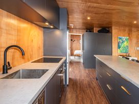 A kitchen with countertops cabinets a black faucet and an induction cooktop with a view into a bedroom in Mountain Haus Ohakune