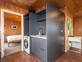 A laundry area with a washing machine and sink next to a doorway leading to a bedroom with a bed at Mountain Haus - Ohakune Holiday Home in Ohakune
