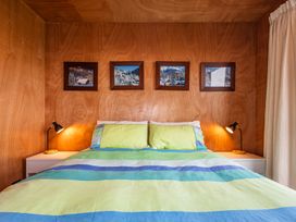 A bedroom with a bed with green blue and white striped bedding two black lamps on white bedside tables and four framed pictures on a wooden wall at Mountain Haus Ohakune
