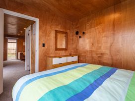 A bedroom with wood panel walls a bed with striped bedding a dresser and a mirror at Mountain Haus Ohakune