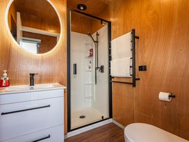 A bathroom with a white vanity and sink a round mirror a shower with glass door a towel rack with two towels and a toilet at Mountain Haus - Ohakune Holiday Home in Ohakune