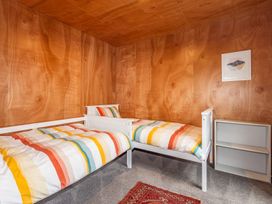 A bedroom with two single beds with striped bedding a small bookshelf and wood paneled walls at Mountain Haus - Ohakune Holiday Home Ohakune