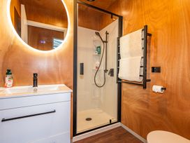 A bathroom with a white sink vanity a round illuminated mirror a glass shower with black fixtures a towel rack with towels and a toilet paper holder at Mountain Haus - Ohakune Holiday Home in Ohakune