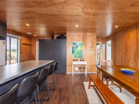An open kitchen and dining area with a countertop and bar stools next to a wooden dining table with benches and chairs at Mountain Haus - Ohakune Holiday Home in Ohakune