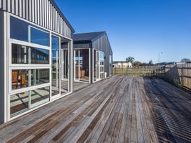 An outdoor wooden deck attached to a modern house with large windows and a fenced yard at Mountain Haus - Ohakune Holiday Home in Ohakune