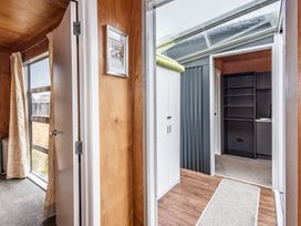 A hallway with wooden paneled walls leading to a room with shelves and a white cabinet at Mountain Haus - Ohakune Holiday Home in Ohakune