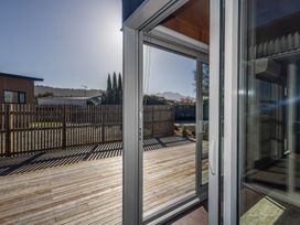 A sliding glass door opening to a wooden deck with a wooden fence and trees in the background at Mountain Haus - Ohakune Holiday Home in Ohakune
