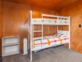 A room with wooden walls and carpeted floor containing a white bunk bed with colorful striped bedding a small white shelf and a portable heater Mountain Haus - Ohakune Holiday Home Ohakune