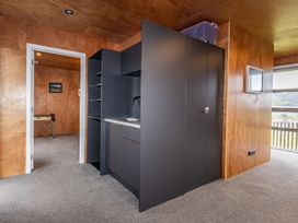 A kitchenette with dark cabinets and a sink in a wood-paneled room with a doorway leading to another room with a foosball table and a framed picture on the wall at Mountain Haus - Ohakune Holiday Home