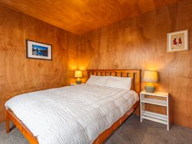 A bedroom with a wooden bed with white bedding two bedside tables with lamps and framed pictures on wood-paneled walls at Mountain Haus - Ohakune Holiday Home in Ohakune