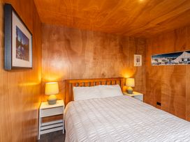 A bedroom with a double bed white bedding wooden walls two bedside tables each with a lamp and framed pictures on the walls at Mountain Haus - Ohakune Holiday Home in Ohakune