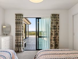 A bedroom with two beds and a sliding door leading to a deck at Island Views - Waihi Beach