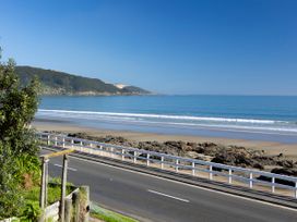 A beach with waves and rocks near a road at Ahipara in Kaitaia