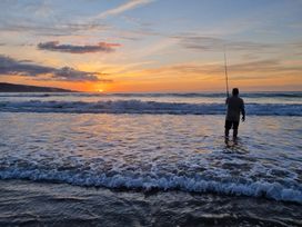 A fisherman standing in the ocean at sunset at Te Hu - Ahipara Beachfront Bach Ahipara