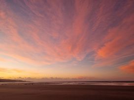 A sunset view of the beach with clouds and ocean at Te Hu - Ahipara Beachfront Bach Ahipara