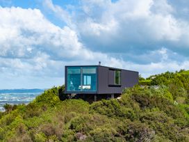 A house on a hill surrounded by bushes at Mangawhai Heads Holiday Home in Mangawhai
