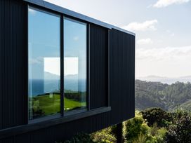 A building with a large window overlooking an ocean and hillside at Mangawhai Heads Holiday Home, Mangawhai