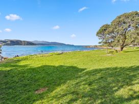 A garden area with grass, a bench, trees, and water at Seaside Nook - Wellington Holiday Home Lyall Bay