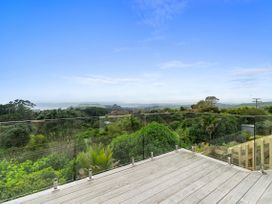 A balcony with a glass railing overlooking trees and the ocean at Raglan Holiday Home in Raglan