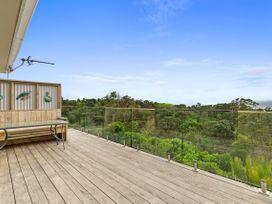 A deck with a bench and railing overlooking trees at Raglan Holiday Home in Raglan