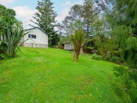 A garden with grass, trees, a house and a shed at Birdsong Retreat - Titirangi Holiday Home Auckland