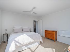 A bedroom with a bed, nightstand, dresser and door at Beachfront Landing - Pauanui Holiday Home Pauanui