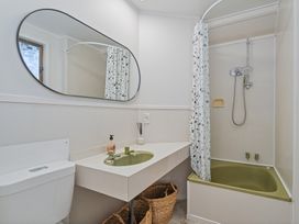 A bathroom with a sink, toilet, mirror, and bathtub at Beachfront Landing - Pauanui