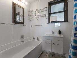 A bathroom with a bathtub, sink, mirror, and shelves at Natives Nest - Karikari Peninsula Escape, Kaitaia