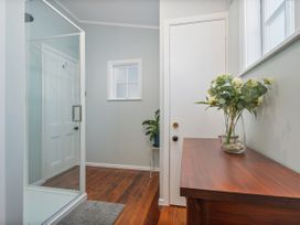 A bathroom with a shower, door, and flowers on a table at Creed Cottage - Whitianga