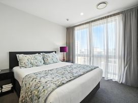 A bedroom with a bed and large windows at Downtown Haven - Christchurch Holiday Apartment Christchurch