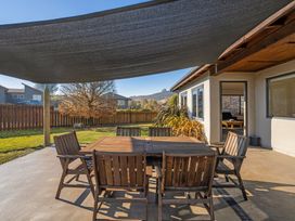 An outdoor area with a table and chairs under a sunshade at Vista Vale - Wanaka Holiday Home