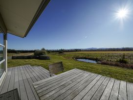 An outdoor deck with a table and chairs overlooking a pond and grassy field at Tussock Cottage - Canterbury