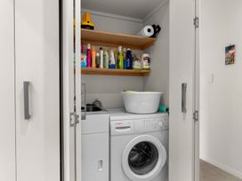A laundry room with a washing machine and cleaning supplies at Mangawhai Heads