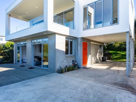 An outdoor area of a house with large windows and orange door at Mangawhai Heads