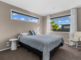 A bedroom with a bed and a chair at Mangawhai Heads Holiday Home in Mangawhai