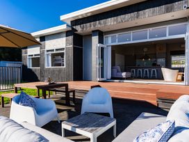 An outdoor patio with chairs and a table facing a house at Mangawhai Heads Holiday Home Mangawhai