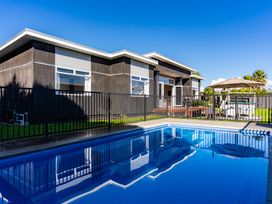 An outdoor area with a swimming pool and a house at Mangawhai Heads Holiday Home in Mangawhai