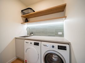 A laundry room with washing machine, dryer, sink and shelf at Te anau Holiday home in Te Anau