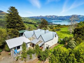 A house surrounded by trees and grass with mountains and a lake in the background at Akaroa Holiday Home