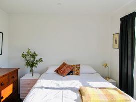 A bedroom with a bed, nightstand, dresser, and plant at Whiritoa Holiday House in Whiritoa