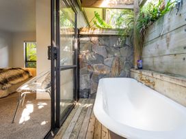 A bathroom with a bathtub and stone wall at Living The Dream - Matarangi Holiday Home Matarangi