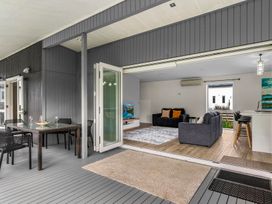 An outdoor patio with a dining table and chairs next to an open living room at Mangawhai Heads Holiday Home Mangawhai Heads