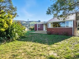 An outdoor view of a red house with grass and plants at Maison Pierre Rouge - Duvauchelle Holiday Home Akaroa