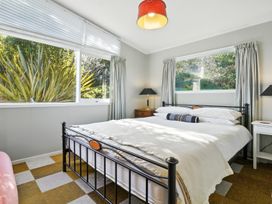 A bedroom with a bed and windows at Maison Pierre Rouge - Duvauchelle Holiday Home Akaroa