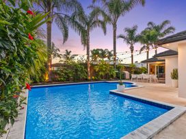 A swimming pool surrounded by palm trees and outdoor furniture at JB's Sanctuary - Papamoa Holiday Home, Papamoa