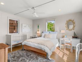 A bedroom with a bed, crib, desk, and lamp at Oli Kai - Algies Bay Holiday Home in Algies Bay