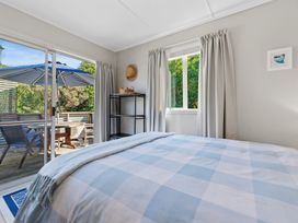 A bedroom with a bed and window leading to outdoor seating at White-Sands Hideaway - Waihi Beach