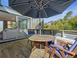 An outdoor area with a table and chairs shaded by an umbrella at White-Sands Hideaway - Waihi Beach